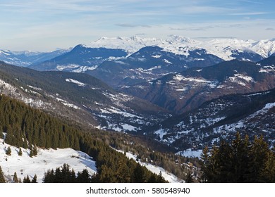Panoramic view down snow covered valley in alpine mountain range with conifer pine trees