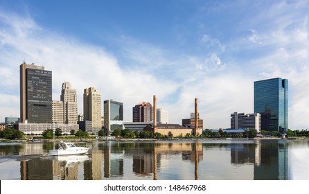 A panoramic view of downtown Toledo Ohio's skyline reflecting into the Maumee river with a power boat cruising by.  A beautiful  blue sky with white clouds for a backdrop.