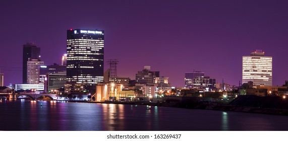 A panoramic view of downtown Toledo Ohio's skyline at night from across the Maumee river.  A beautiful  purple sky with the city lights reflecting into the Maumee river.