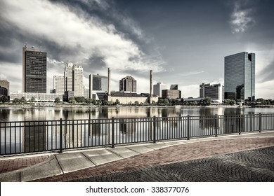 A panoramic view of downtown Toledo Ohio's skyline from across the Maumee river at a popular restaurant area with a paver brick boardwalk and a decorative iron railing..