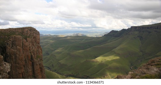 Panoramic view of the dramatic Lesotho Sani Mountains with deep valleys, green slopes, and rocky cliffs under a partly cloudy sky. Breathtaking highland landscape captured from a scenic viewpoint, showcasing the raw natural beauty and vast scale of southern African mountains. Ideal for travel, adventure, and landscape themes.