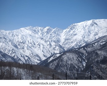 Panoramic view of dramatic snow-capped mountain peaks rising above a forest valley under a clear blue sky in winter