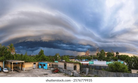 A panoramic view of a dramatic storm cloud formation over a small town with lush greenery and industrial structures