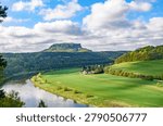 Panoramic view of the Elbe river bend in Saxon Switzerland with the historic Lilienstein mountain, beautiful green fields and rural village landscape under a cloudy blue sky, Germany