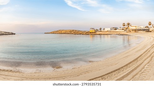 Panoramic view of empty sandy Vathia Gonia beach with tire tracks near calm sea bay in morning light in December. Coastal resort landscape. Ayia Napa, Cyprus.