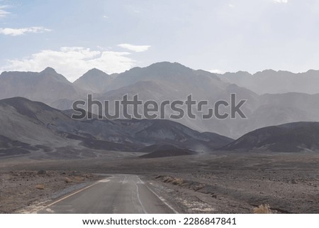 Panoramic view of endless empty road leading to colorful geology of multi hued Artist Palette rock formations in Death Valley National Park near Furnace Creek, California, USA. Black mountains