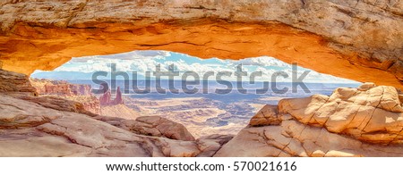 Panoramic view of famous Mesa Arch, iconic symbol of the American West, illuminated golden in beautiful morning light on a sunny day with blue sky and clouds, Canyonlands National Park, Utah, USA