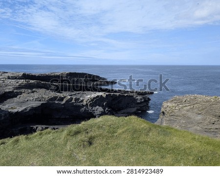 Panoramic view of flat, stratified rock platforms meeting the deep blue waters of the Atlantic Ocean on the Irish coast.