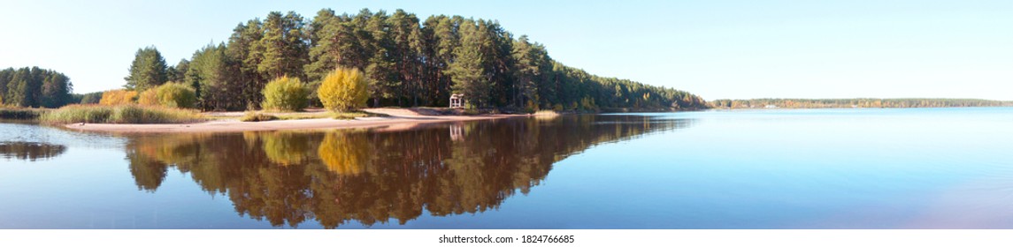 Panoramic view of the forest island, pond or lake. The reflection in the water. Beautiful widescreen autumn landscape.