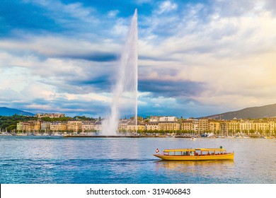 Panoramic view of Geneva skyline with famous Jet d'Eau fountain and traditional boat at harbor district in beautiful evening light at sunset, Canton of Geneva, Switzerland