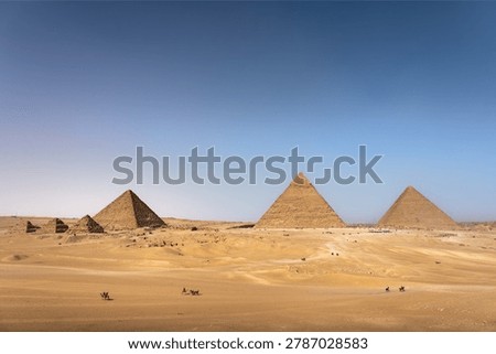 Panoramic view of the Giza pyramid complex with camel riders crossing the desert plateau, Cairo, Egypt
