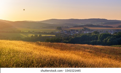 Panoramic view of golden grass ears, beautiful countryside and sun setting over rolling hills. Beauty in nature concept. Hot air baloon in the air in background - Powered by Shutterstock