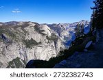 Panoramic view of granite cliffs and mountain landscape in Yosemite National Park under clear blue sky.
