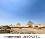 Panoramic view of the Great Pyramids of Giza with surrounding ruins and sand landscape under bright clear skies in Egypt. High quality photo