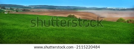 panoramic view of green fields winter wheat and clouds of dust on the hills of plowed lands, problem of soil erosion from the wind
