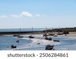 Panoramic view of the harbor of Barmouth, UK during low tide with boats on the sandbanks of the Mawddach Estuary and Afon Mawddach river against a white clouded blue sky