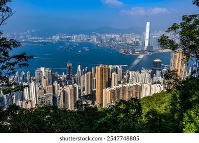 A panoramic view of Hong Kong dense cityscape, showcasing towering skyscrapers and a lush green hillside. The blue sky with a single fluffy cloud provides a picturesque backdrop. - Powered by Shutterstock