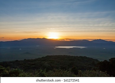 Panoramic view of huge Ngorongoro caldera (extinct volcano crater) with setting Sun against evening glow background at dusk. Great Rift Valley, Tanzania, East Africa. 