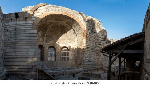 Panoramic view inside the Thermes de Constantin in Arles, France, featuring a massive barrel vault, brick arch, stone walls, and restored windows in the ancient bath complex.