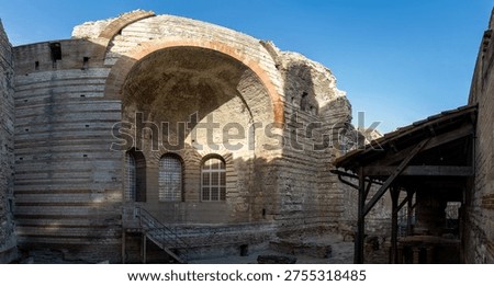 Panoramic view inside the Thermes de Constantin in Arles, France, featuring a massive barrel vault, brick arch, stone walls, and restored windows in the ancient bath complex.