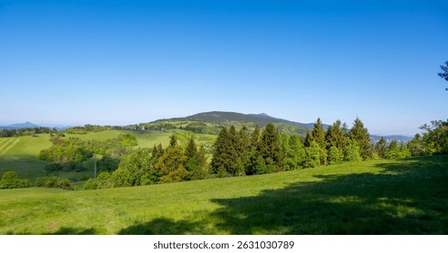 Panoramic view of Jested mountain with its iconic tower on the top, surrounded by green meadows, scattered cottages and small villages in the Czech countryside