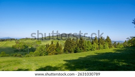 Panoramic view of Jested mountain with its iconic tower on the top, surrounded by green meadows, scattered cottages and small villages in the Czech countryside