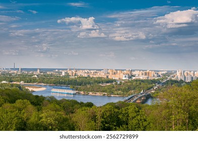 A panoramic view of Kyiv featuring the majestic Dnipro River, lush greenery, and vibrant city architecture under a clear sky. - Powered by Shutterstock