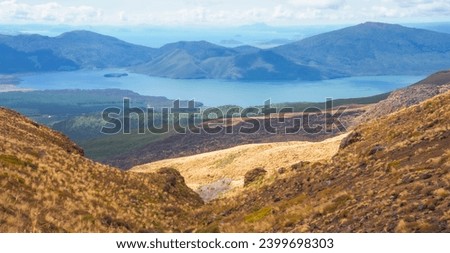 Panoramic view of Lake Taupo in New Zealand's volcanic plateau. Emerald waters cradle lush greenery, a vibrant blue sky dotted with cotton-candys completes this picture of serene beauty.