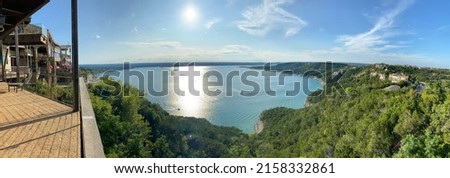 A panoramic view of the Lake Travis surrounded with trees from a view point under cloudy sky in Austin