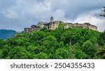 Panoramic view Landskron Castle in Villach, Carinthia, Austria. Majestic fortress perched atop verdant forest covered hill. Imposing structure with fortified walls, towers and prominent church spire