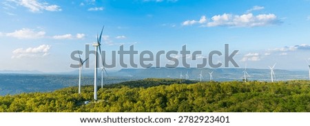Panoramic view of a large wind farm with turbines on green hills. Renewable energy production and clean technology landscape under blue sky with clouds.