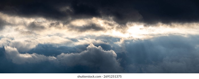 Panoramic view of layered dramatic storm clouds with a burst of sunlight breaking through the upper dark layer, as a symbol of hope and the power of nature