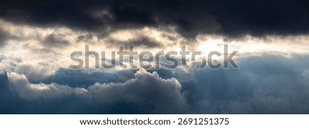Panoramic view of layered dramatic storm clouds with a burst of sunlight breaking through the upper dark layer, as a symbol of hope and the power of nature