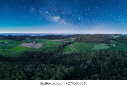 Panoramic view of lush fields and forests under a starlit sky at twilight in the countryside