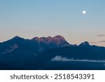 Panoramic view of majestic snow-capped mountain peak Mittagskogel (Kepa) at full moon in Karawanks seen from Rosental, Carinthia, Austria. Tranquil alpine landscape in peaceful Austrian Alps in winter