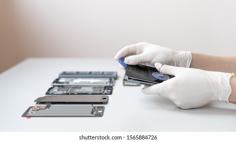 Panoramic view of man showing process of mobile phone repair, using tool equipment to change damaged touch screen on smartphone. Repairman working behind table with copy space
