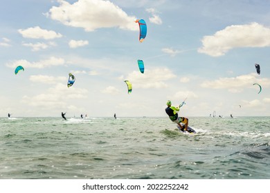 Panoramic view of many people enjoy riding kite surf board in sun uv protection suit on bright sunny day at sea or ocean shore kitesurfing camp spot. Watersport adrenaline fun adventure acitivity