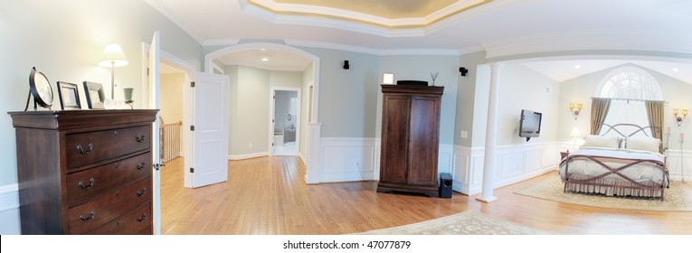 Panoramic view of a master suite interior, containing a bed and dressers. Horizontal format.