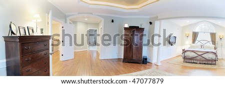 Panoramic view of a master suite interior, containing a bed and dressers. Horizontal format.