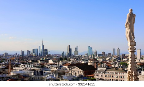 Panoramic View Of Milan Skyline From Duomo Cathedral. Religious Statue Faces To The Buildings Of The Financial District. The Alps Mountains On The Background.