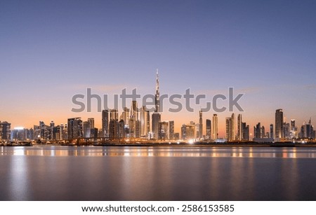 A panoramic view of Dubai’s modern skyline at sunset, showcasing towering Burj Khalifa and Business Bay shimmering skyscrapers mirrored on tranquil waters. 