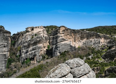 Panoramic view of the Monastery of Varlaam dramatically built atop towering rock formations in Meteora, Greece. This UNESCO World Heritage site showcases the unique blend of natural geology and historic Orthodox monastic architecture.