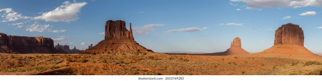 Panoramic view of Monument Valley featuring towering red sandstone buttes and mesas under a clear blue sky, typical of the American Southwest desert landscape.