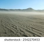 Panoramic view of Mount Bromo with expanse of cliffs and blue sky. A wide expanse of sandy sea with a little grass starting to turn green