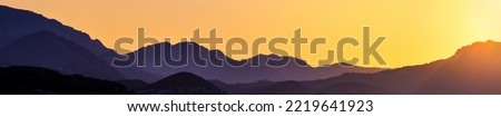 Panoramic view of mountain layers on golden sunset. Silhouettes of blue hills with gradient sunlight. Wide mountain landscape for a concept of hiking template background on a flyer or billboard.