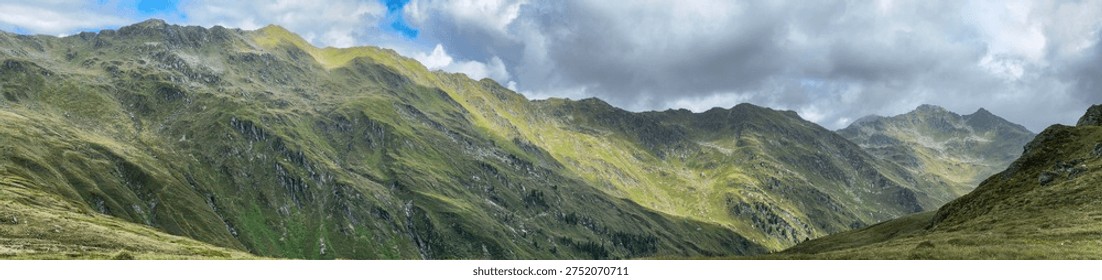Panoramic view of a mountain range in Königsleiten Austria during the summer The landscape features green slopes and rocky peaks under a cloudy sky creating a scenic outdoor environment.
