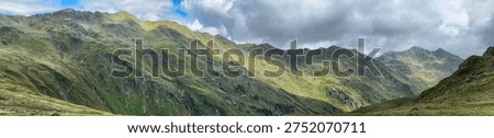 Panoramic view of a mountain range in Königsleiten Austria during the summer The landscape features green slopes and rocky peaks under a cloudy sky creating a scenic outdoor environment.
