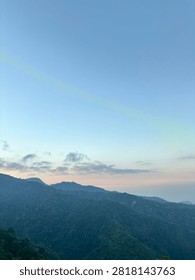 Panoramic view of mountain range silhouette under a clear blue sky at early dawn or twilight.