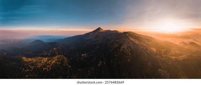Panoramic view of a mountain range at sunset with vibrant colors and clear blue sky, showcasing natural beauty and tranquility.