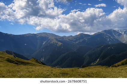 A panoramic view of a mountain range under a partly cloudy sky.  Rolling green hills in the foreground lead the eye to the distant, majestic peaks.